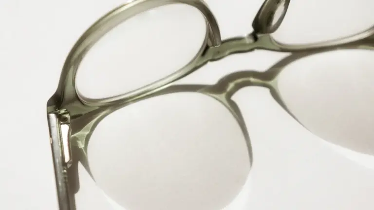 Gros plan sur une paire de lunettes à monture claire sur fond blanc minimaliste.