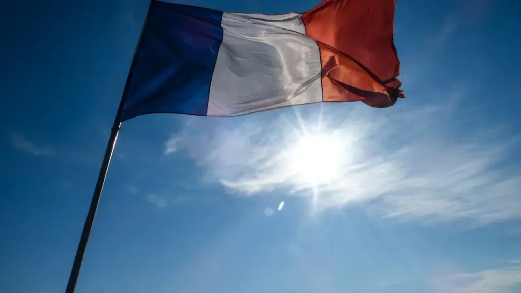 Drapeau tricolore français flottant sous un ciel bleu ensoleillé et lumineux.