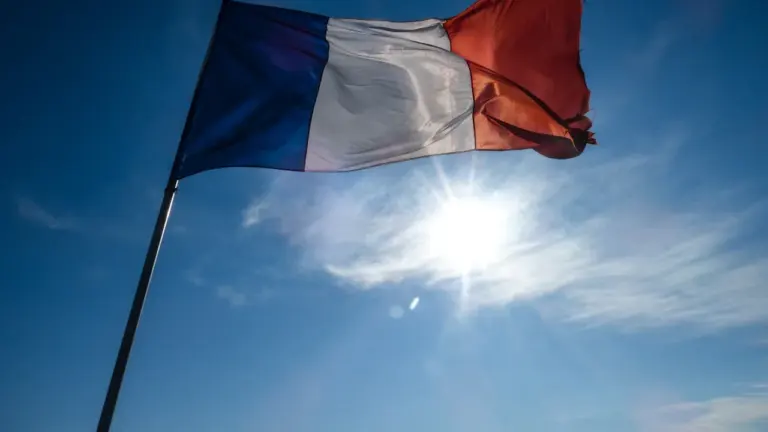 Drapeau tricolore français flottant sous un ciel bleu ensoleillé et lumineux.