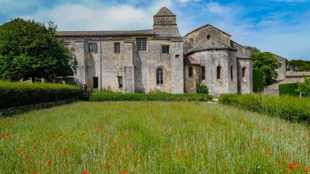 Vue extérieure d'une ancienne abbaye en pierre bordée d'un champ de coquelicots sauvages.