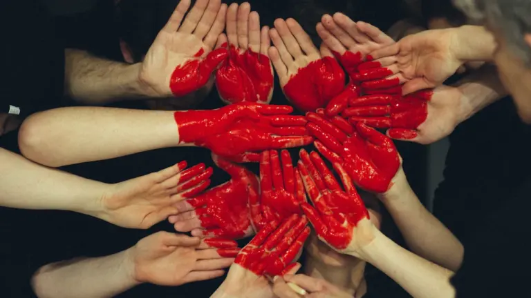Mains humaines peintes en rouge symbolisant le don de sang et la solidarité.