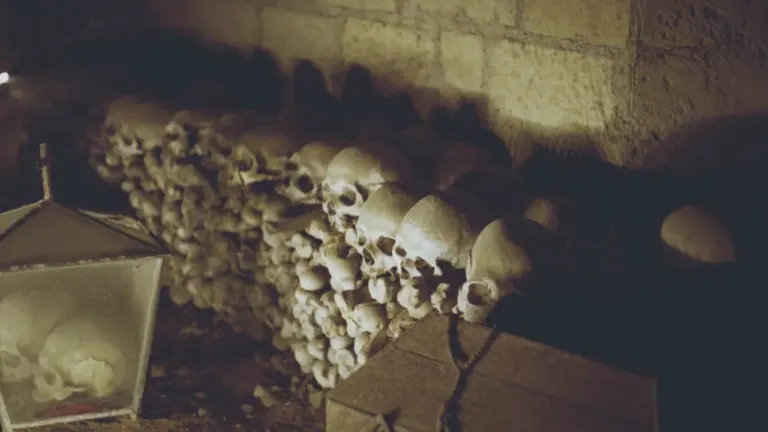 Mur d'ossements et crânes humains conservés dans une crypte ancienne sombre et historique.