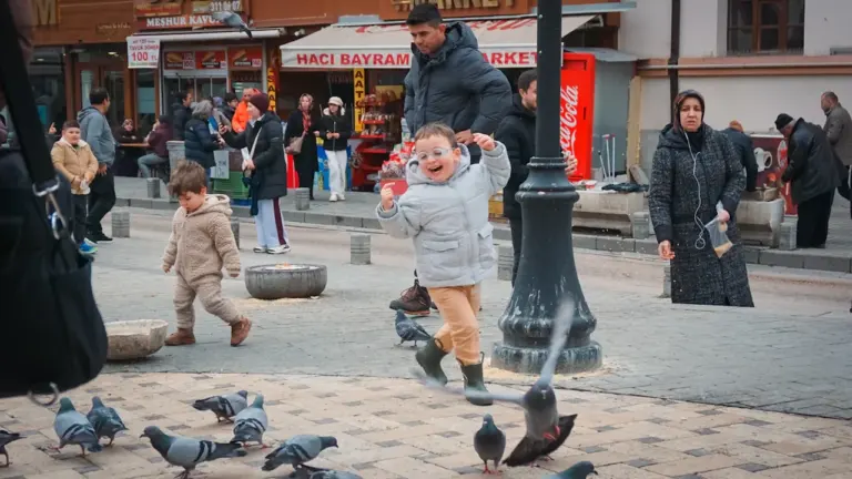 Un enfant joyeux court après des pigeons sur une place publique animée en ville.