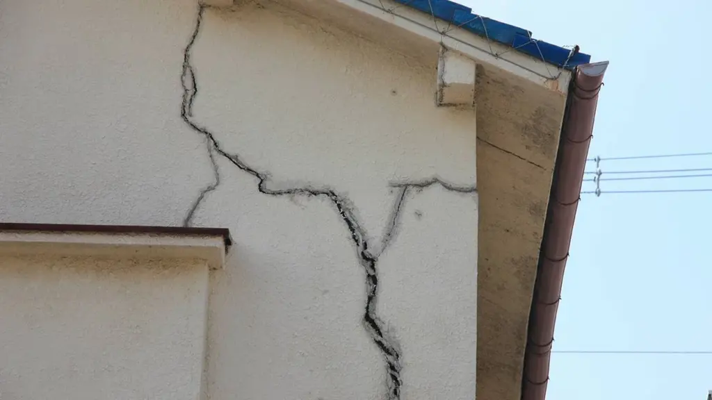 Vue rapprochée d'une façade de maison beige présentant des fissures structurelles importantes et profondes.