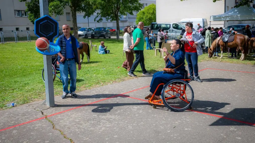 Une femme en fauteuil roulant participe à une activité sportive extérieure avec un ballon basket.